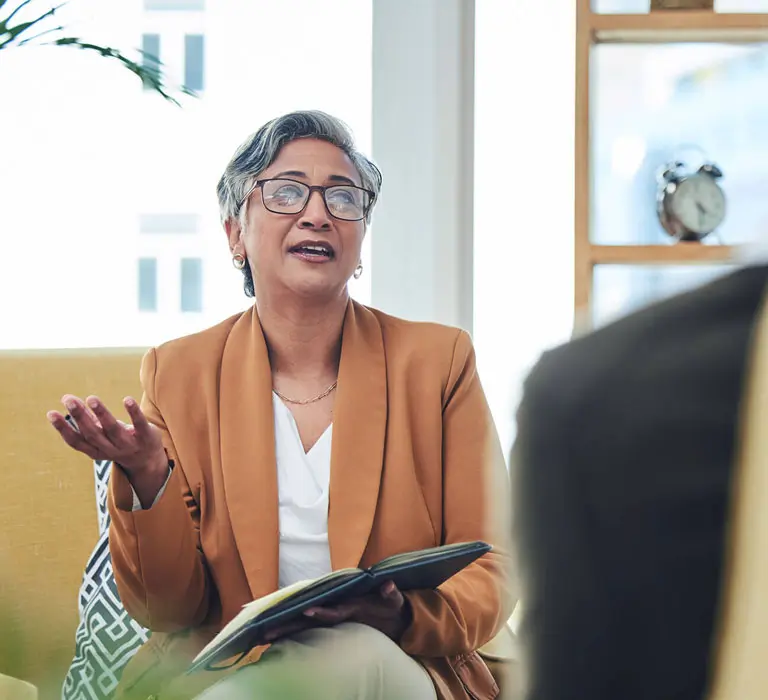 A counselor holding a notepad speaking to a client.