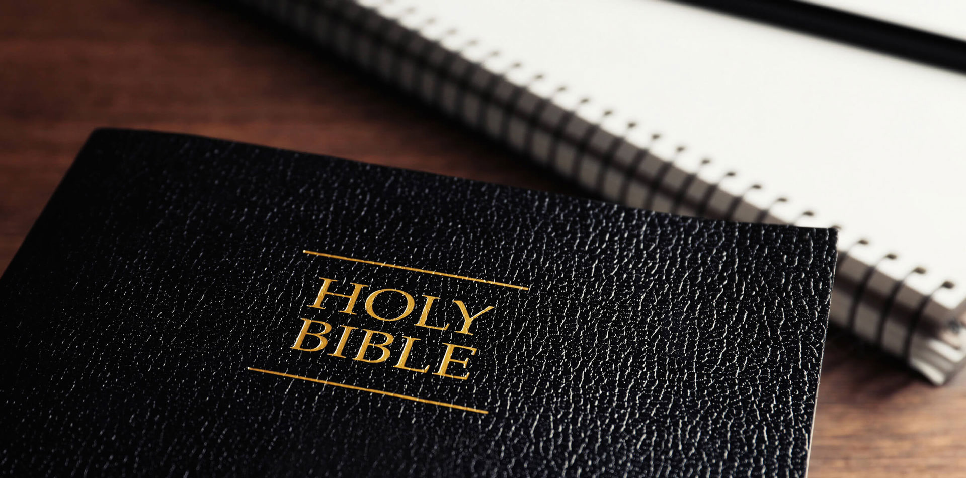 A black Bible on a table next to a notepad and pen