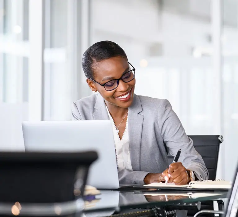 Woman with laptop writing notes on desk